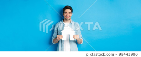 Insurance, mortgage and real estate concept. Smiling young man holding house model, searching apartment for rent, standing against blue background Insurance, mortgage and real estate concept. Smiling young man holding house model, searching apartment for rent, standing against blue background 98443990