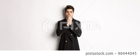 Portrait of shocked handsome businessman in suit, reacting to terrible situation, gasping and covering mouth with hands, standing startled against white background Portrait of shocked handsome businessman in suit, reacting to terrible situation, gasping and covering mouth with hands, standing startled against white background 98444045