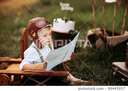 Little pilot boy in vintage aviator hat attentively studying map near the wooden plane outdoor  98445057