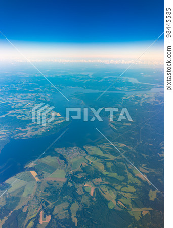 Aerial view from airplane window above green ground. View from the airplane window with beautiful clouds at sunrise Aerial view from airplane window above green ground. View from the airplane window with beautiful clouds at sunrise 98445585