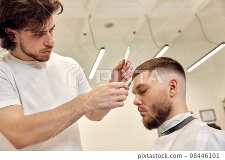 hairdresser does haircut for caucasian bearded man 98446101