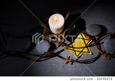 Holocaust memory day. Barbed wire, stones, yellow star and burning candle on black background 98446859