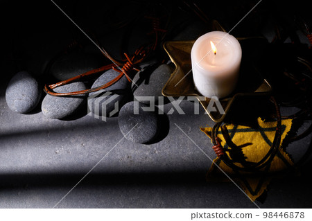 Holocaust memory day. Barbed wire, stones, yellow star and burning candle on black background 98446878