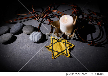 Holocaust memory day. Barbed wire, stones, yellow star and burning candle on black background 98446880