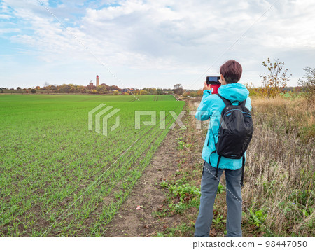 Woman takes photo of field with Cape Arkona lighthouse. Baltic Sea 98447050