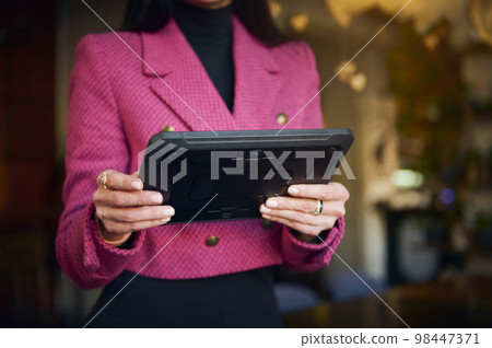 Details on digital tablet in the hands of a restaurateur, businesswoman in bright purple casual wear, executive director or successful manager, CEO against blurred background of a restaurant interior 98447371