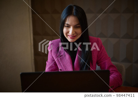 Smiling confident woman entrepreneur 40-45 years old, dressed in a stylish crimson jacket, talking to business clients via video link. Successful entrepreneur at online meeting with business partners 98447411