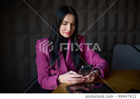 Beautiful confident Caucasian 40-45 years old woman, successful businesswoman in formal wear, chatting on mobile phone while waiting for colleagues and business partners for meeting in office interior 98447412