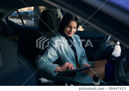 Confident Caucasian businesswoman sitting on driver's seat, using digital tablet, working on new project, telecommuting, planning meeting with colleagues. Lifestyle People Remote work business concept Confident Caucasian businesswoman sitting on driver's seat, using digital tablet, working on new project, telecommuting, planning meeting with colleagues. Lifestyle People Remote work business concept 98447413