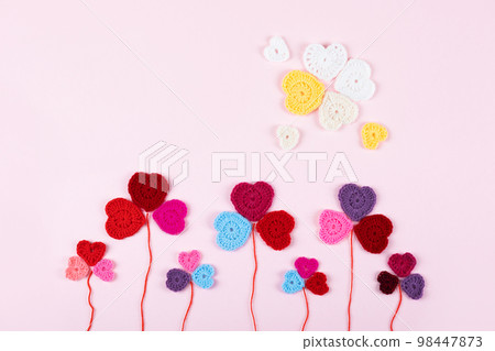 Multicolored crocheted hearts are laid out in the shape of a flower clover on a lilac background. Happy Valentine's Day, Mother's Day and birthday greeting card. 98447873
