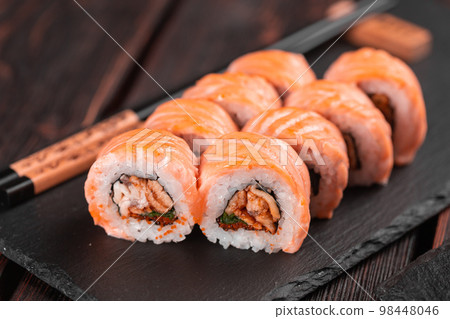 Sushi roll maguro with salmon, smoked eel, avocado and tobiko on black board close-up. Sushi menu. Japanese food. Sushi roll maguro with salmon, smoked eel, avocado and tobiko on black board close-up. Sushi menu. Japanese food. 98448046