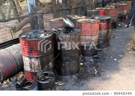 Old rusty barrel left in the road leaking thick black tar or oil on an urban street in Kolkata, India 98448349
