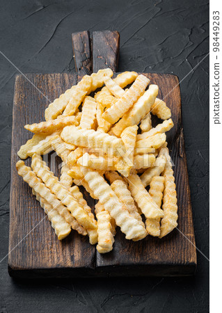Frozen fries, on wooden cutting board, on black background Frozen fries, on wooden cutting board, on black background 98449283