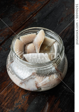 Pickled herring, in glass jar, on old dark  wooden table background. 98449291