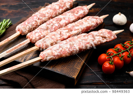 Raw Lula kebab on skewers, with grill ingredients, on old dark  wooden table background 98449363