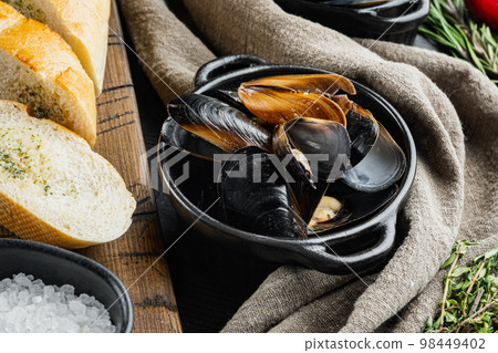 Traditional seafood mussels in wine sauce and baguette toasts, on black wooden table background Traditional seafood mussels in wine sauce and baguette toasts, on black wooden table background 98449402