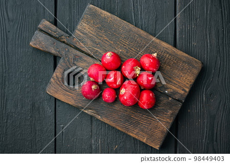 Bunch of ripe radishes, on wooden cutting board, on black wooden table background, top view flat lay Bunch of ripe radishes, on wooden cutting board, on black wooden table background, top view flat lay 98449403