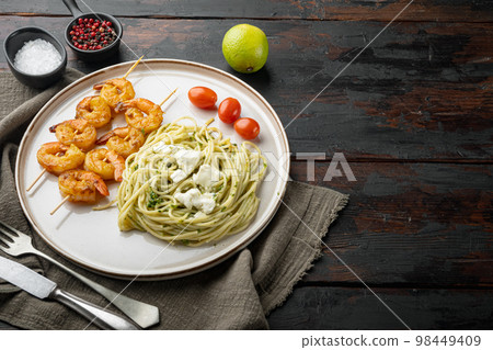 Green spaghetti with pesto sauce and grilled shrimp skewers, on plate, on old dark wooden table background , with copyspace and space for text Green spaghetti with pesto sauce and grilled shrimp skewers, on plate, on old dark wooden table background , with copyspace and space for text 98449409