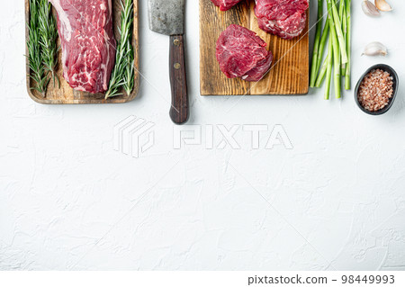 Raw beef fillet steaks with herbs and spices with whole tenderloin fillet cut, in cast iron frying pan, on white stone  background, top view flat lay, with copy space for text 98449993