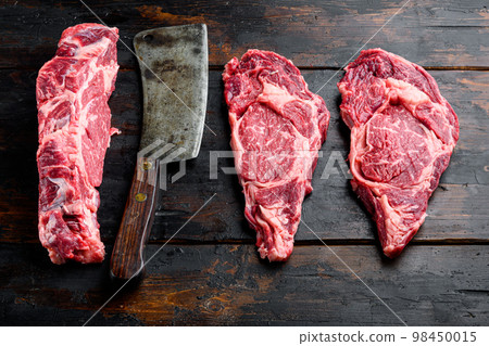 Rib eye beef steak raw, and old butcher cleaver knife, on old dark wooden table background, top view flat lay Rib eye beef steak raw, and old butcher cleaver knife, on old dark wooden table background, top view flat lay 98450015
