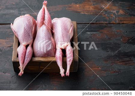 Raw uncooked quails , on dark wooden background  with space for text 98450048