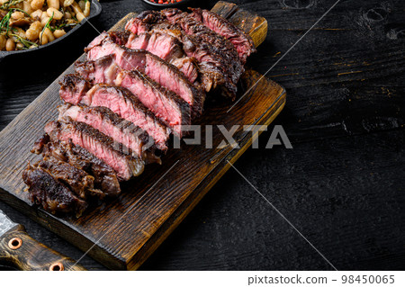 Sliced medium rare grilled Beef steak, rib eye cut, on wooden serving board, with copy space for text 98450065