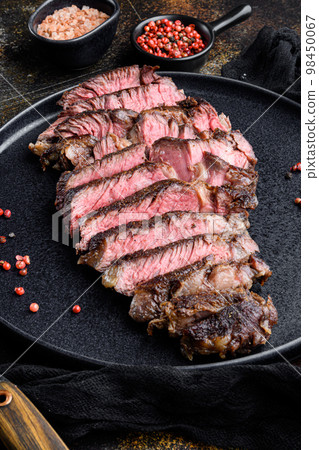 Juicy medium beef Rib Eye steak slices, on plate, on old dark rustic background Juicy medium beef Rib Eye steak slices, on plate, on old dark rustic background 98450067
