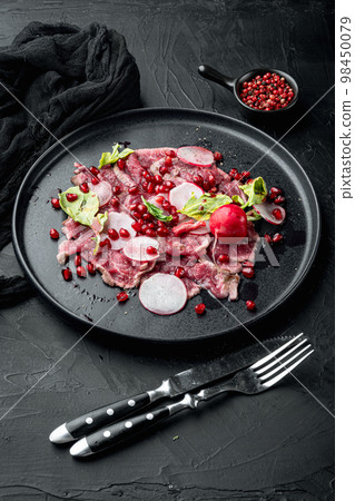 Carpaccio beef, with Radish and garnet, on plate, on black stone background 98450079
