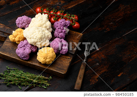 Purple yellow and white cauliflower, on cutting board, on old dark  wooden table background, with copy space for text 98450185