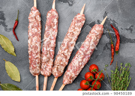 Raw kofta meat kebabs sausages, with grill ingredients, on gray stone table background, top view flat lay Raw kofta meat kebabs sausages, with grill ingredients, on gray stone table background, top view flat lay 98450189