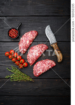 Uncooked minced meat beef burger cutlets, on black wooden table background, top view flat lay Uncooked minced meat beef burger cutlets, on black wooden table background, top view flat lay 98450195