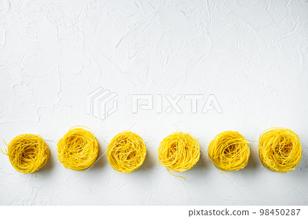 Dried taglierini , on white stone surface, top view flat lay, with copy space for text Dried taglierini , on white stone surface, top view flat lay, with copy space for text 98450287