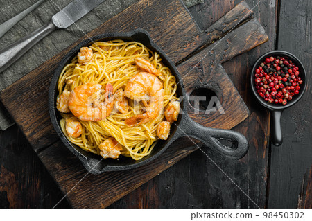 Tasty appetizing pasta spaghetti with pesto sauce and shrimps, in cast iron frying pan, on old dark  wooden table , top view flat lay 98450302