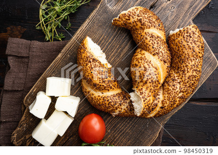 Simit or gevrek, traditional Turkish pastry food with breakfast ingredients olive and tomato cheese , on old dark  wooden table background, top view flat lay 98450319
