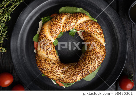 Simit bagel sandwich with lettuce, tomato, cheese, on black wooden table background, top view flat lay Simit bagel sandwich with lettuce, tomato, cheese, on black wooden table background, top view flat lay 98450361