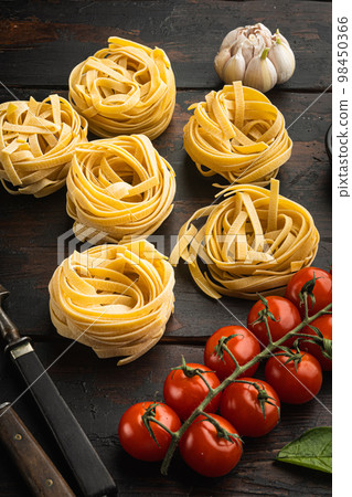 Fettuccine Tagliatelle pasta Italian food ingredients, on old dark wooden table background Fettuccine Tagliatelle pasta Italian food ingredients, on old dark wooden table background 98450366