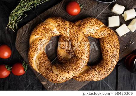 Turkish bagel Simit with sesame with breakfast ingredients olive and tomato cheese, on black wooden table background, top view flat lay Turkish bagel Simit with sesame with breakfast ingredients olive and tomato cheese, on black wooden table background, top view flat lay 98450369