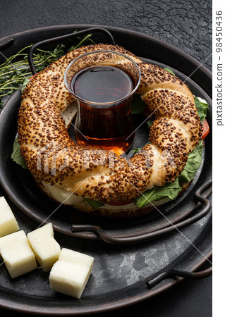 Fast Turkish breakfast Simit with cheese and greenswith glass of turkish black tea with glass of turkish black tea, on black dark stone table background Fast Turkish breakfast Simit with cheese and greenswith glass of turkish black tea with glass of turkish black tea, on black dark stone table background 98450436