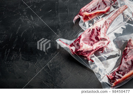 Raw uncooked beef steaks in vacuum packed air sealed sous vide bag, tomahawk, t bone and club steak cuts, on black stone background, with copy space for text 98450477