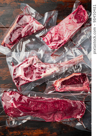 Vacuum packed organic raw beef classic cuts, tomahawk, t bone, club steak, rib eye and tenderloin cuts, on old dark wooden table background Vacuum packed organic raw beef classic cuts, tomahawk, t bone, club steak, rib eye and tenderloin cuts, on old dark wooden table background 98450481