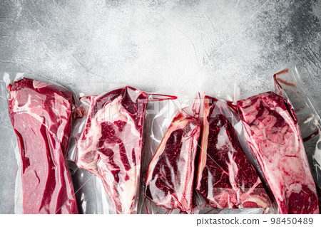 Raw marbled beef steak in vacuum packaging, tomahawk, t bone, club steak, rib eye and tenderloin cuts, on gray stone background, top view flat lay, with copy space for text Raw marbled beef steak in vacuum packaging, tomahawk, t bone, club steak, rib eye and tenderloin cuts, on gray stone background, top view flat lay, with copy space for text 98450489