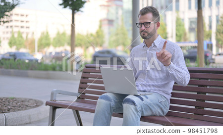 Rejecting Young Adult Man in Denial While using Laptop Sitting Outdoor on Bench Rejecting Young Adult Man in Denial While using Laptop Sitting Outdoor on Bench 98451798