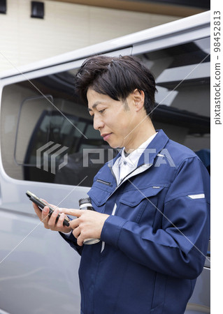 A worker man checking a smartphone in front of a work vehicle 98452813