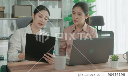 Two young enthusiastic businesswoman working together in the office workspace. 98456196