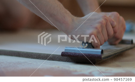 Carpenter grinders sanding wooden board. Close up of hands 98457169