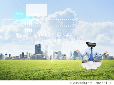 Camera headed man sitting in lotus pose on cloud against modern cityscape 98464127