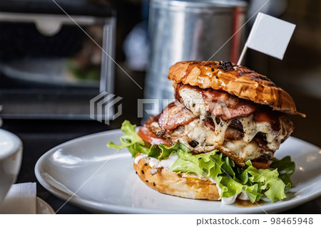 Delicious grilled beef and ham burger with lettuce and mayonnaise on a wooden table in a cafe, with copy space Delicious grilled beef and ham burger with lettuce and mayonnaise on a wooden table in a cafe, with copy space 98465948