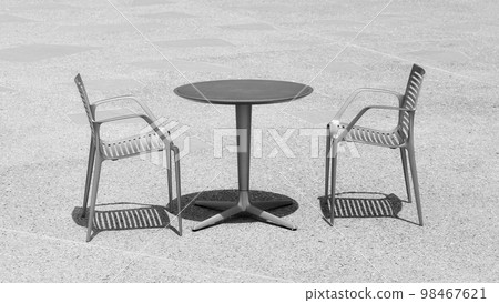 Black and white photo of two chairs at an empty table, selective focus. 98467621