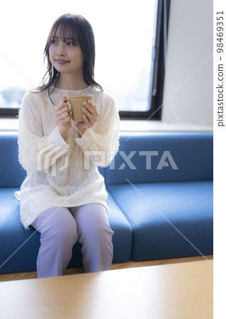 Woman relaxing on the sofa in the office with a cup of coffee. looking at something 98469351
