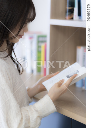 Young woman reading while looking for a book on a bookshelf in the office. Young woman reading while looking for a book on a bookshelf in the office. 98469379